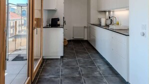 Eine schmale Küche mit weißen Schränken, einer schwarzen Arbeitsplatte und einem gefliesten Boden.