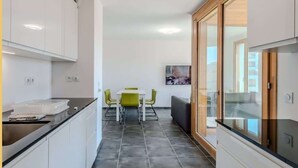 Eine moderne Küche mit weißen Schränken, einer schwarzen Arbeitsplatte und einem Essbereich mit weißem Tisch und grünen Stühlen.