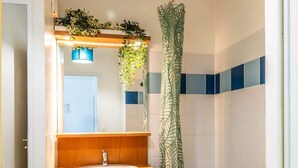 A bathroom with a wooden vanity, a sink, a mirror, a shower with a green leaf-patterned curtain, and a tiled wall with blue accents.