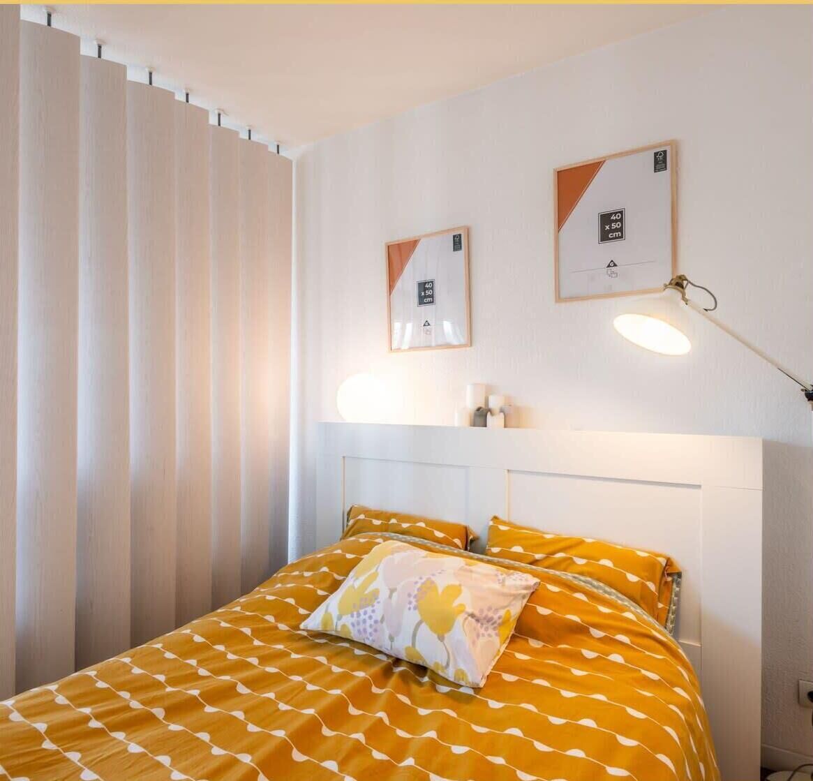 A hotel room with a bed, a nightstand, a lamp, and a window with curtains.