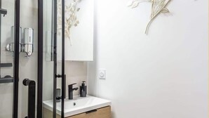 Ett modernt badrum med en duschavdelning i glas, en vit tvättställ med svarta detaljer och ett träskåp.