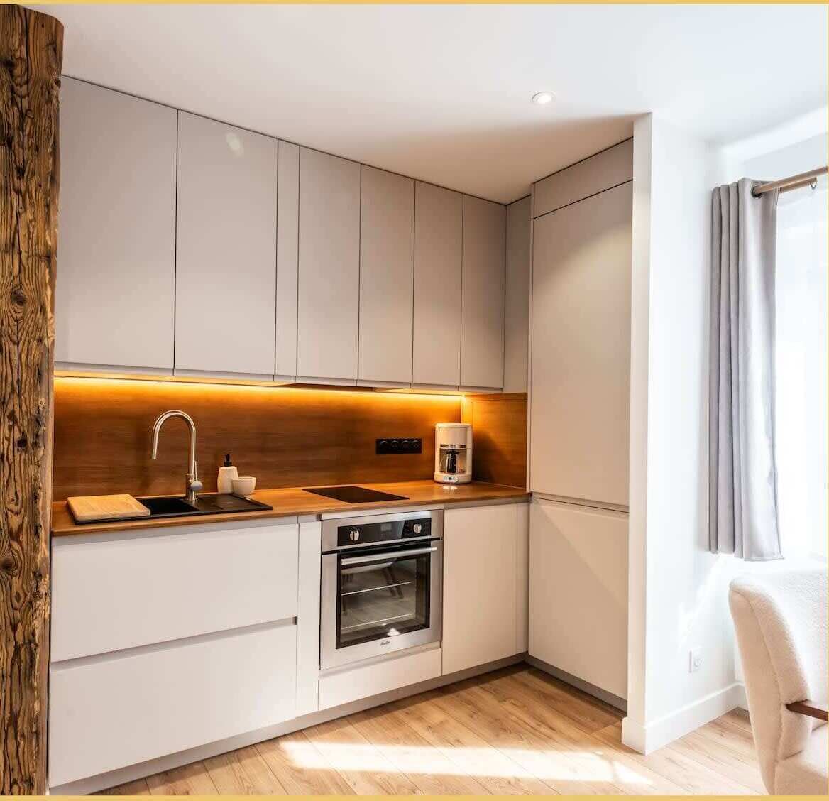 Eine moderne Küche mit weißen Schränken, einem eingebauten Ofen, einer Kaffeemaschine und einer Wand mit Holzvertäfelung.