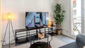 Ett modernt vardagsrum med en platt-TV, ett soffbord i glas, en soffa, en golvlampa och en krukväxt.