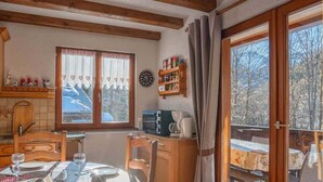 Un comedor acogedor con una mesa lista para dos, un armario de madera con utensilios de cocina y una vista de una montaña nevada a través de una ventana.