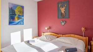 Un dormitorio con cama de madera, ropa de cama blanca, pared roja y dos lámparas fijadas a la pared.