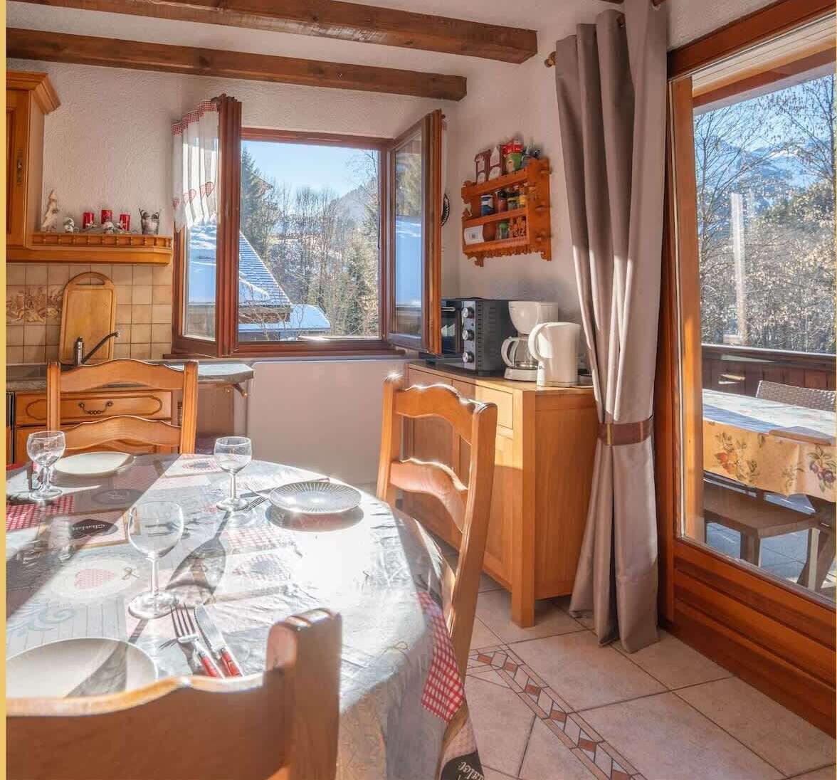 Un comedor acogedor con una mesa dispuesta para dos, sillas de madera, una ventana con cortinas y vistas al exterior.