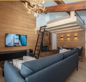 A modern living room with a wooden interior, a fireplace, a TV mounted on the wall, and a staircase leading to an upper level. - The Nest - Votre cocon alpin à Megève (Megève)