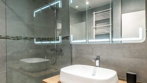 Une salle de bain moderne avec un grand miroir, un lavabo blanc et une cabine de douche en verre.