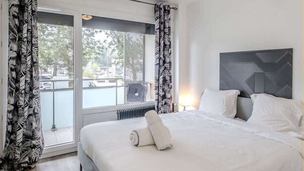 Une chambre d’hôtel moderne avec un grand lit, une vue sur l’extérieur et une œuvre d’art géométrique accrochée au mur.