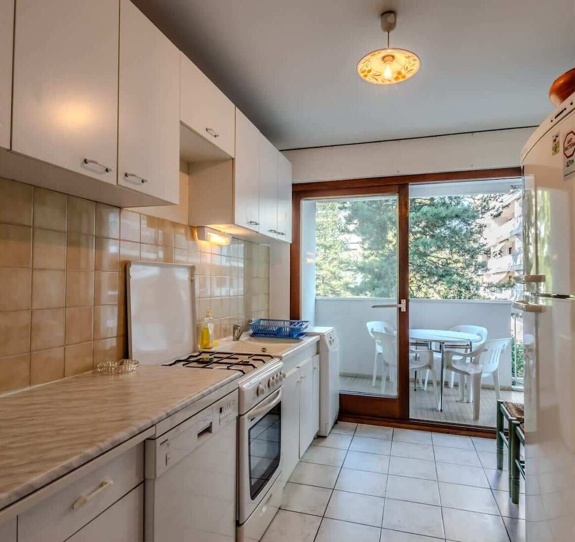Una cocina moderna con armarios blancos, estufa a gas y horno empotrado. Hay una ventana con vistas a zonas verdes.