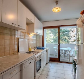 A modern kitchen with white cabinets, a gas stove, and a built-in oven. There is a window with a view of greenery outside.