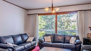 Ein Wohnzimmer mit zwei schwarzen Ledersofas, einem Holztisch und einem großen Fenster mit Balkonblick.