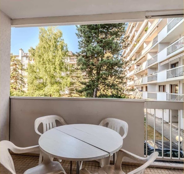 A balcony with a round table and four chairs, overlooking a residential area with trees and multi-story buildings.