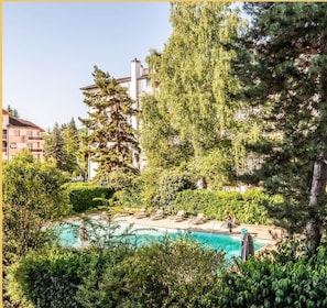 A pool surrounded by lush greenery and tall trees, with a building in the background.