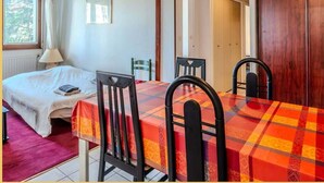 Ein Zimmer mit einem Bett, einem Tisch mit Stühlen, einem Fenster mit Vorhängen und einer Tür zu einem weiteren Raum.