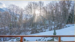 En träveranda med ett bord och stolar, med utsikt över ett snötäckt landskap med träd och berg.
