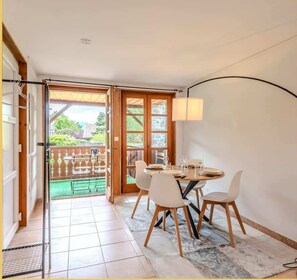 Un coin repas avec une table dressée pour quatre personnes, une porte-fenêtre coulissante donnant sur une terrasse extérieure et une vue sur le jardin.