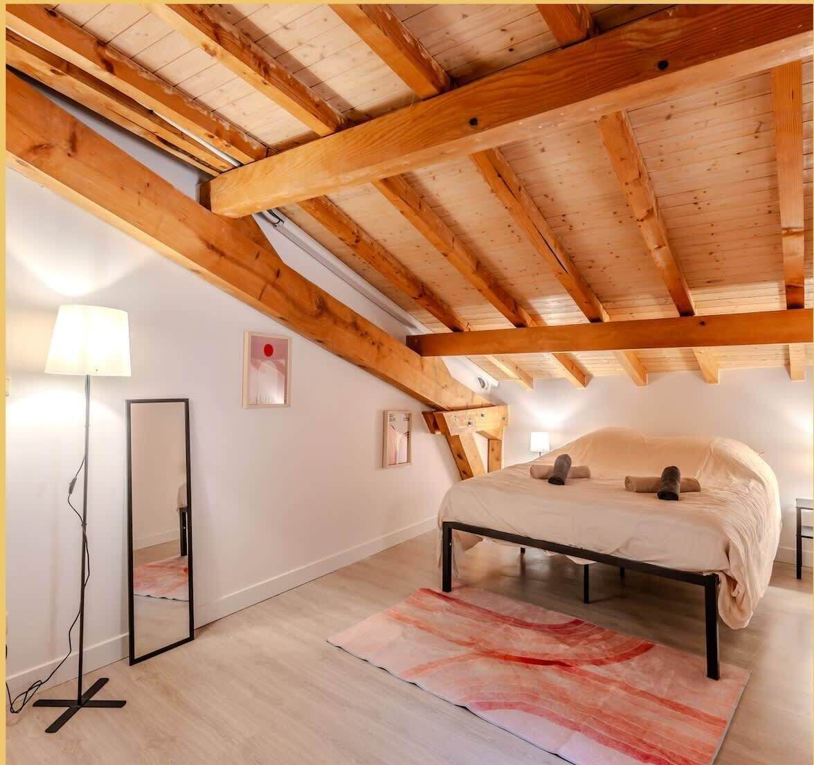 A bedroom with a wooden ceiling, a bed, a floor lamp, and a mirror.