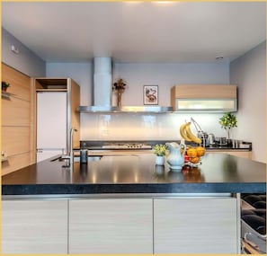 A modern kitchen with a central island, stainless steel appliances, and light wood cabinetry.