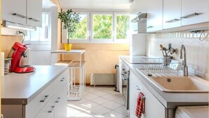 A modern kitchen with white cabinets, a red coffee maker, a sink with utensils, and a potted plant. - Chez Amel & Val I T2 I Annemasse (Annemasse)