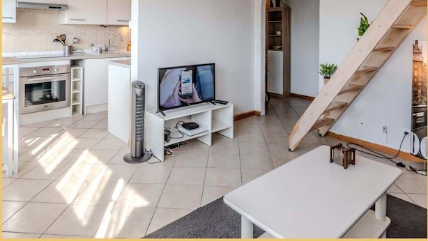 A modern kitchen with white cabinets, a built-in oven, and a TV on a white stand. - Chez Amel & Val I T2 I Annemasse (Annemasse)