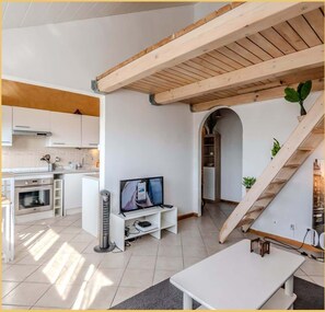 Une cuisine moderne avec des meubles blancs, un four encastré et un téléviseur posé sur un meuble blanc.