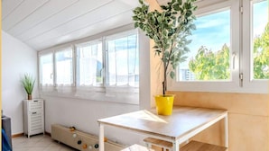 A bright room with a white ceiling, large windows, a radiator, and a table with a potted plant. - Chez Amel & Val I T2 I Annemasse (Annemasse)