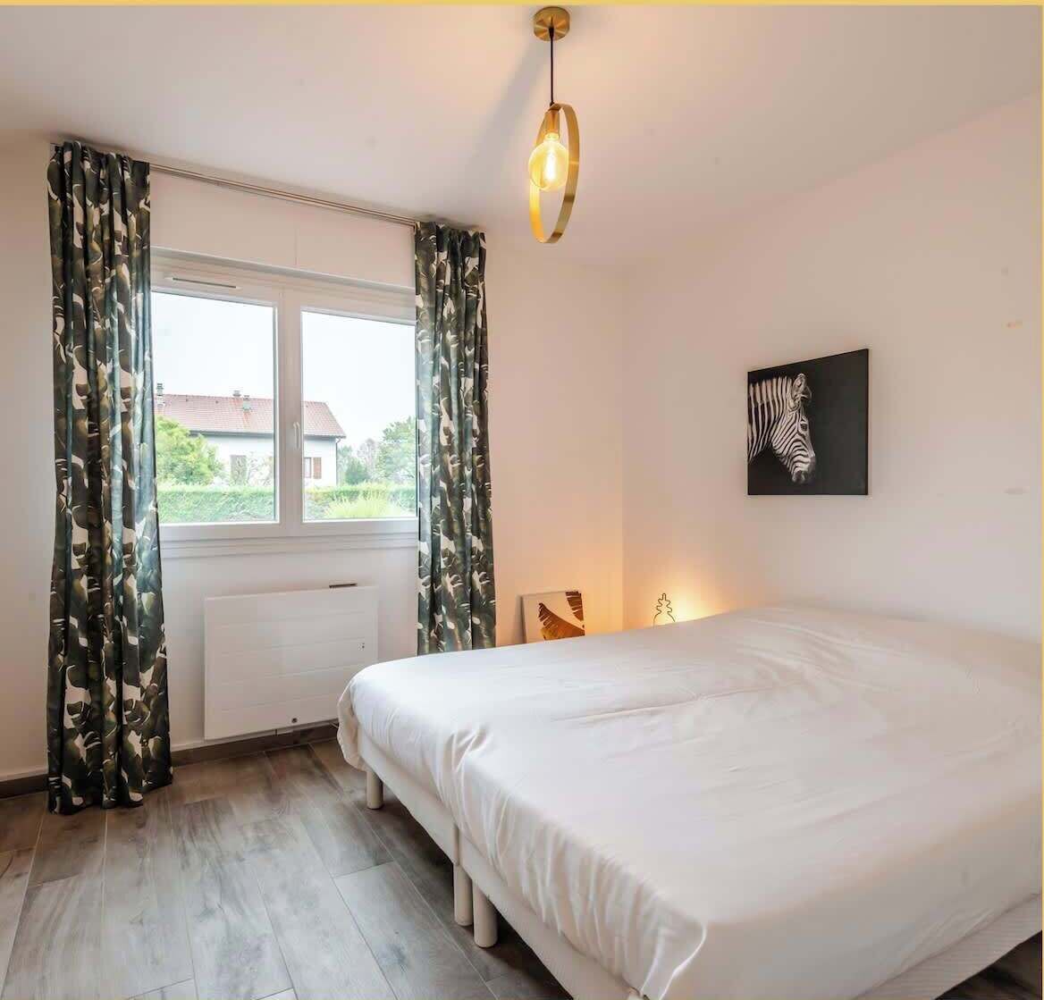 A bedroom with a large bed, a radiator, a window with curtains, and a zebra artwork on the wall.