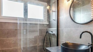 Une salle de bain moderne avec un grand lavabo noir, un miroir rond et un espace douche.