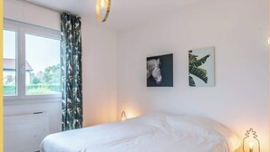Une chambre avec un grand lit, une fenêtre avec des rideaux et deux œuvres d’art accrochées au mur.