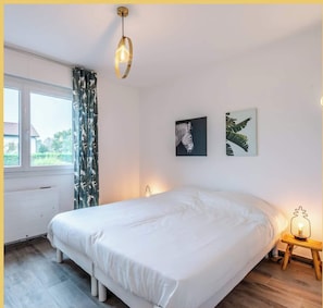 A bedroom with a large bed, a window with curtains, and two wall-mounted artworks.