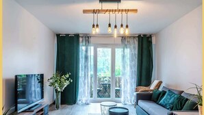 Un salon moderne doté d’un téléviseur à écran plat, d’un canapé, d’une table basse et d’un coin repas visible à travers une porte en verre.