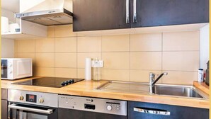 A modern kitchen with dark cabinets, a stainless steel sink, a built-in oven, and a microwave.