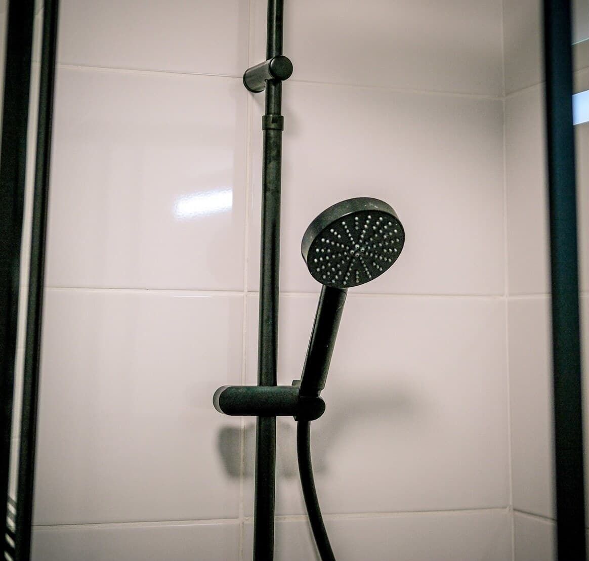 A showerhead with a circular head and a black handle, mounted on a wall with white tiles.