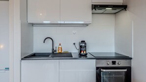 A compact kitchen with white cabinets, a black countertop, a coffee maker, and a built-in oven.