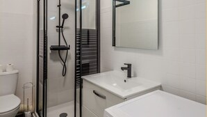 A modern bathroom with a glass-enclosed shower, a white sink, and a large mirror.