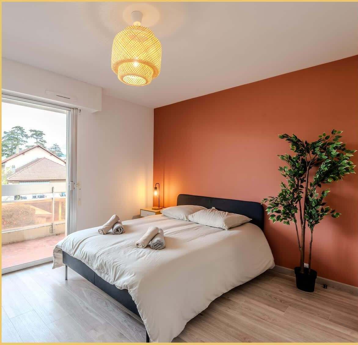 Ein Schlafzimmer mit Bett, Nachttischlampe, Zimmerpflanze und Blick durch eine Schiebetür.