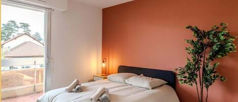 Ein Schlafzimmer mit Bett, Nachttischlampe, Zimmerpflanze und Blick durch eine Schiebetür.