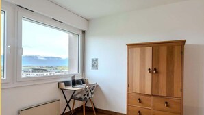 A room with a large window, a wooden cabinet, and a desk with a chair.