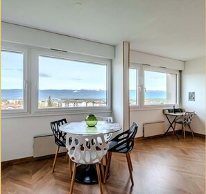 A modern room with large windows, a round table with chairs, and a view of the sea and mountains. - Chez Fan & Alex | St Julien (Saint-Julien-en-Genevois)