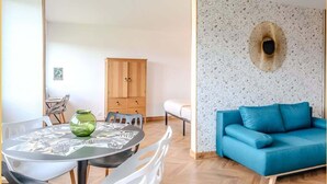 A modern living room with a blue sofa, a dining table with chairs, and a wooden cabinet.