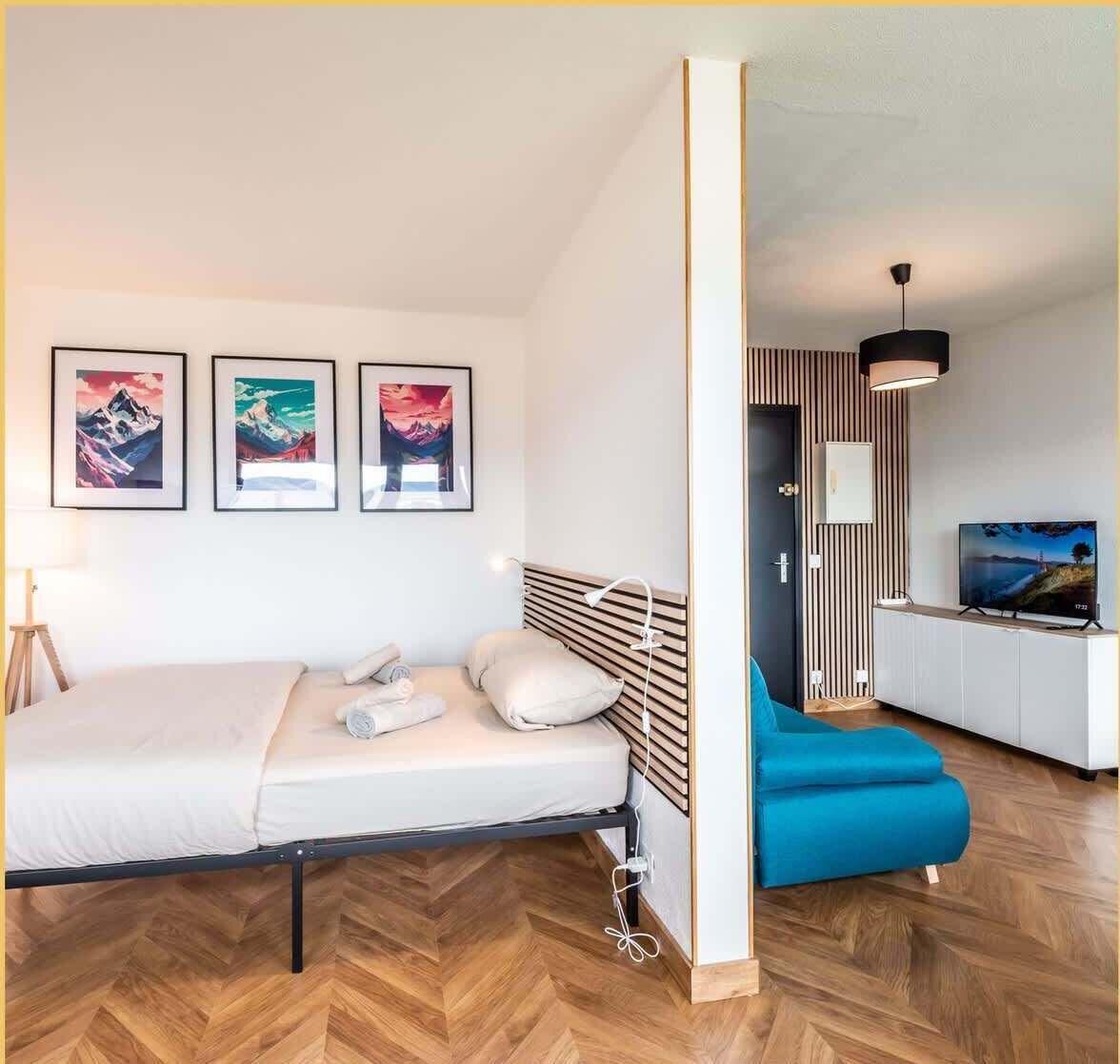 A modern hotel room with a bed, a desk, a TV, and three framed pictures on the wall.