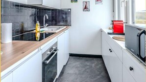 A compact kitchen with a black tiled backsplash, white cabinets, a wooden countertop, a stainless steel sink, a red toaster, and a microwave.