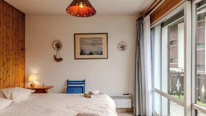Un dormitorio con una cama grande, una lámpara colgante, un cuadro enmarcado y una ventana con cortinas.