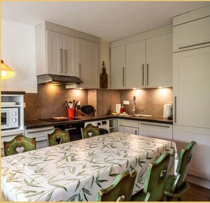 Une cuisine de taille réduite avec des meubles blancs, un four à micro-ondes et une table à manger avec des chaises.