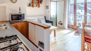 Une cuisine compacte équipée d’un four à micro-ondes, d’une cuisinière et de meubles en bois. On y trouve un petit coin repas avec un banc et une fenêtre donnant sur un balcon.