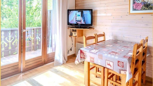 Une pièce aux murs lambrés, avec un téléviseur posé sur un meuble, une table à manger entourée de chaises et une porte-fenêtre coulissante donnant sur un espace extérieur.