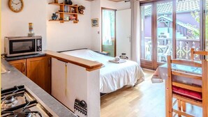 Une pièce compacte comprenant un lit, une petite kitchenette, un plafond en bois et une porte-fenêtre coulissante donnant sur un balcon extérieur.