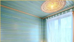 Une chambre à coucher avec un lit, des oreillers, une table de chevet avec une lampe, une fenêtre avec un rideau et un luminaire suspendu au plafond, fait de fibres tressées.