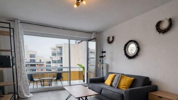 Ein modernes Wohnzimmer mit Sofa, Couchtisch und Bett. Ein Balkon bietet Blick auf die Stadt.